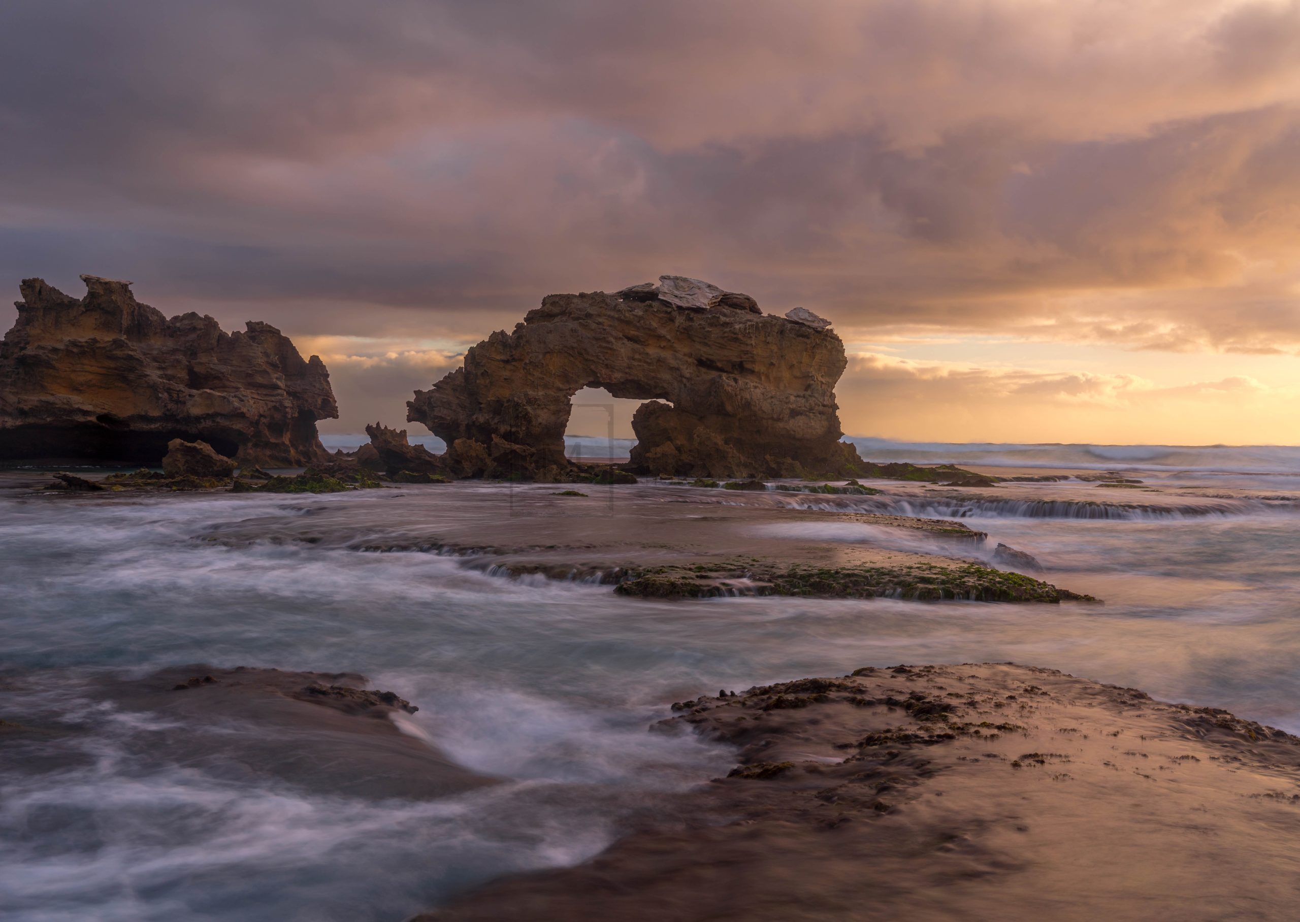 Large rock with hole on ocean beach during sunset